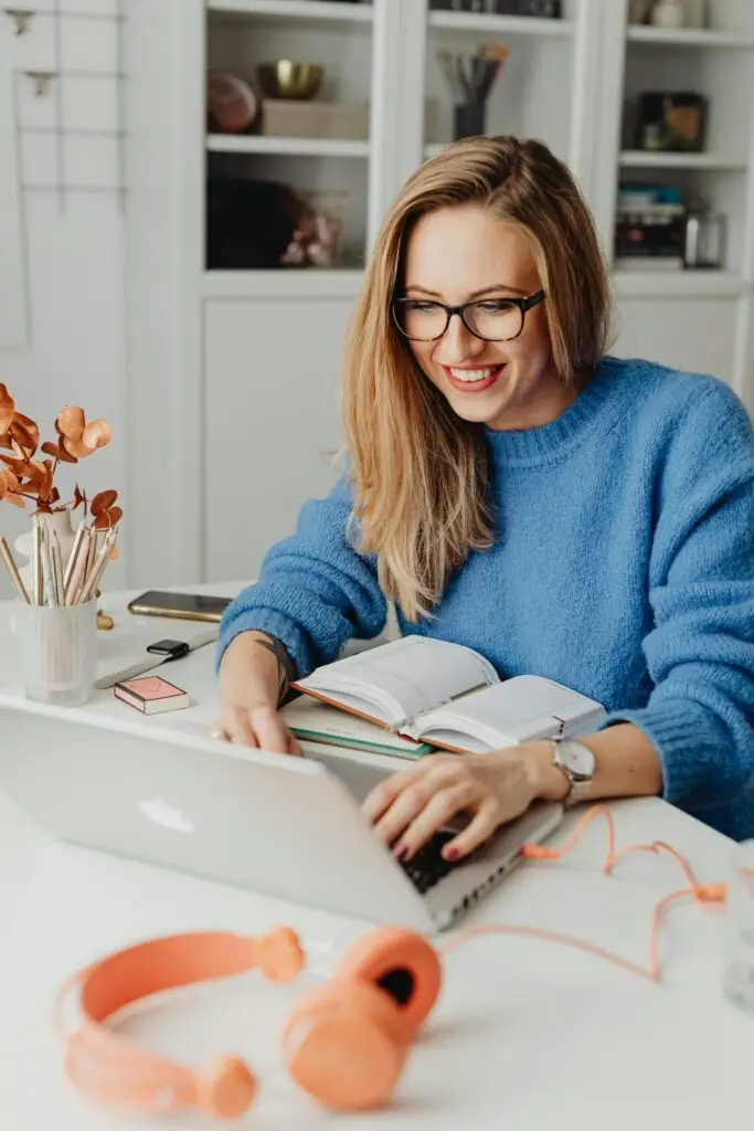 Home 1 A cheerful woman in a blue sweater working remotely with a laptop in a cozy home setting. Home IT Support